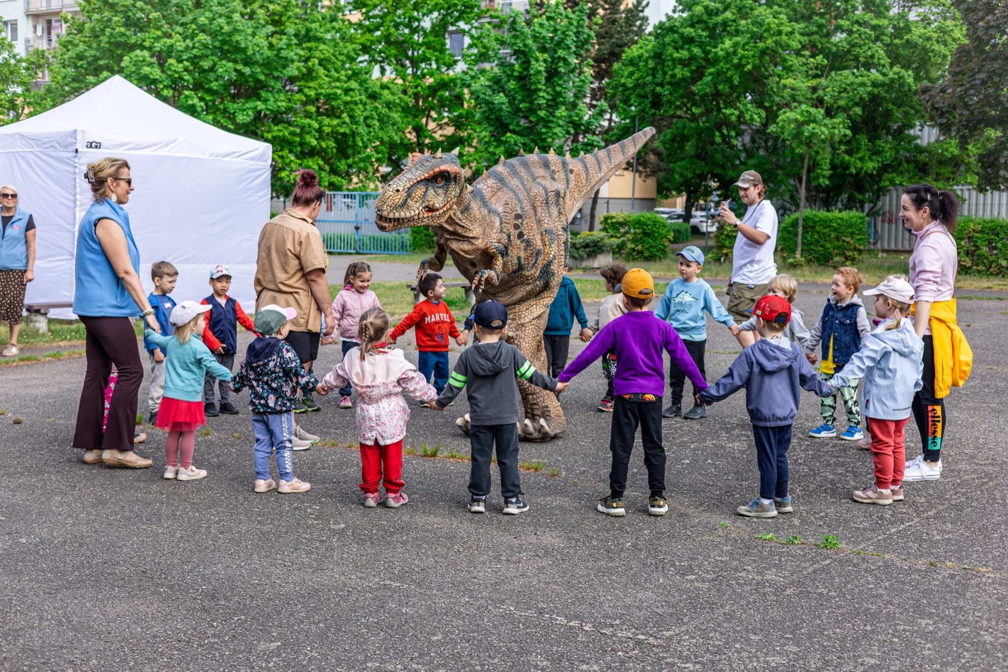 Děti z mateřské školy stojí v kruhu kolem dinosaura